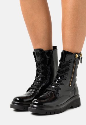 Bottines en cuir verni noir avec des lacets et une fermeture éclair sur le côté, dotées d'une semelle épaisse noire et d'une finition texturée.