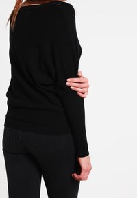 Svart stickad tröja med en avslappnad passform, med en bred halsringning och subtila axeldetaljer. Matchad med svarta jeans.