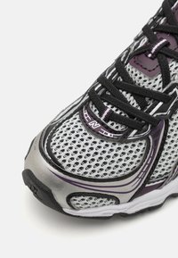 Baskets de course en maille grise avec des lacets noirs, des accents violets et un revêtement synthétique texturé. Elles présentent une semelle rembourrée et des zones de ventilation.