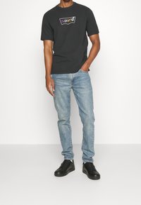 Camiseta negra de manga corta con un logo multicolor de Levi's, combinada con unos jeans claros desgastados y zapatillas negras.