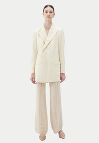 Veste blazer crème croisée avec revers à cran et poches avant, associée à un pantalon beige en maille à jambe large avec un motif texturé.