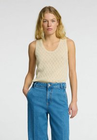 Beige strikket tanktop med et struktureret m�ønster, parret med højtaljede blå denimbukser med lommer og knaplukning.