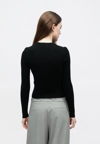 Camisola justa preta com mangas compridas e decote redondo, combinada com calças de cintura alta cinza claro. Textura suave, design minimalista.