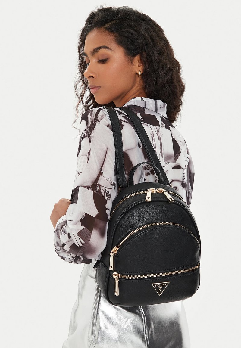 Sac à dos en cuir noir avec deux compartiments zippés, des accents en métal doré et un logo triangulaire. Texture lisse et forme arrondie.