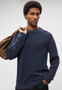 Camisola de malha canelada azul marinho com decote redondo e mangas compridas, apresentando tecido texturizado e corte descontraído. Combinada com uma mala castanha.