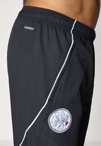 Sorte atletiske shorts lavet af letvægtsstof, med en hvid sidestribe og et broderet Ajax-logo ved kanten. Elastisk talje.