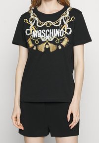 Svart bomullströja med ett grafiskt tryck i guld och silver som föreställer syverktyg samt ordet "Moschino" i fetvita bokstäver.