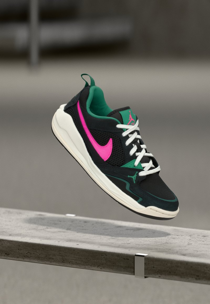 Sneaker nera con texture a rete, accenti verdi, logo rosa, suola bianca e lacci. Presenta una forma distintiva con colletto imbottito.