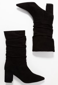 Czarne zamszowe botki za kostkę o luźnym kroju, z ostro zakończonym noskiem i słupkowym obcasem. Charakteryzują się miękką teksturą i gładką powierzchnią.