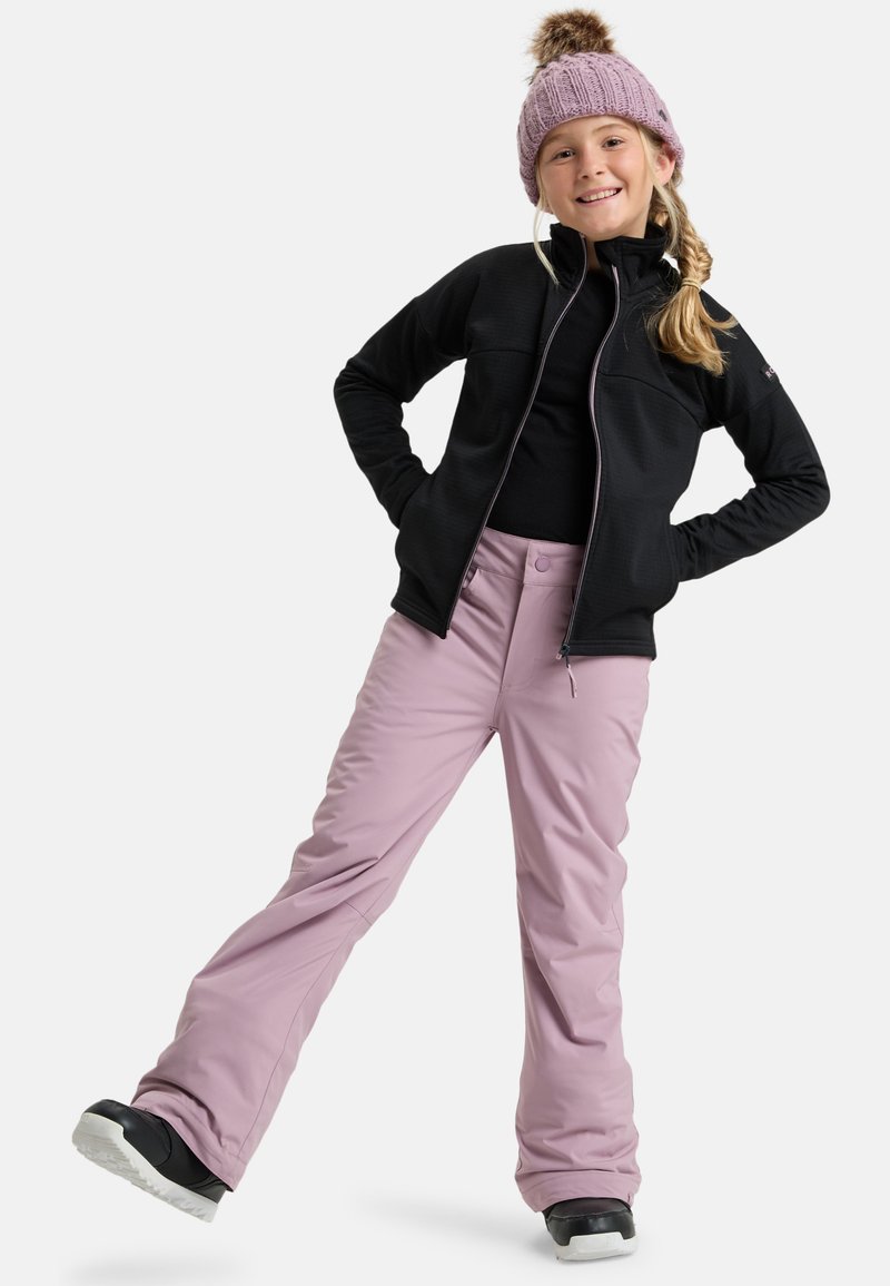 Černá fleecová bunda na zip, černý top, světle levandulové lyžařské kalhoty a černé zimní boty. Růžová pletená čepice z vlny s detailem pom-pom.