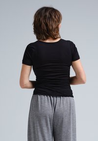 Musta tiukka t-paita lyhyillä hihoilla ja pyöreällä kaula-aukolla, yhdistettynä löysiin harmaisiin pyjama-housuihin. Pehmeä kangas, minimalistinen muotoilu.