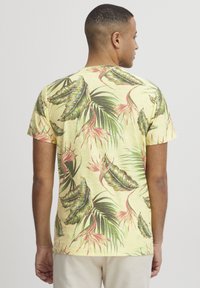 Camiseta de manga corta amarilla con un patrón de hojas y flores tropicales en verde y rosa, con un cuello redondo y un corte relajado.
