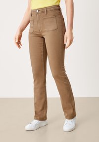 Brązowe, dopasowane dżinsy o średnim stanie, z przednimi i tylnymi kieszeniami oraz jednym zapięciem na guzik. Połączone z białymi sneakersami.