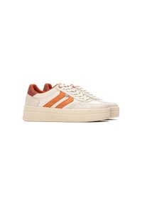 Zapatillas de color crema con dos rayas naranjas, diseño de cordones y un contrafuerte trasero acolchado en tono marrón. Suela de plataforma gruesa con detalles de costura.