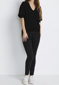 Sort strikket V-hals sweater med puffærmer og tekstureret detalje, parret med sorte skinny jeans og hvide sneakers.