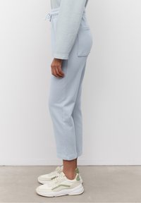 Světle modré tepláky s elastickým pasem, bočními kapsami a manžetami na kotnících, spárované se smetanově bílými a zelenými teniskami. Hladký povrch.