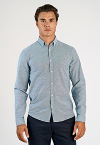 Ανοιχτό μπλε πουκάμισο από απαλό ύφασμα με μακριά μανίκια και γιακά, με λευκά κουμπιά και στυλ στενής γραμμής.