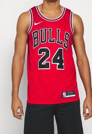 Mies, joka pukeutunut punaiseen Chicago Bullsin koripallopaitaan, jossa numero 24, yhdistettynä mustiin shortseihin, seisoo valkoista taustaa vasten.