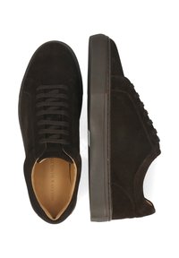 Ett par mörkbruna mockaskor, där den ena visar ovansidan med snören, medan den andra har en sidovy med tjock gummisula och beige inre foder synligt.