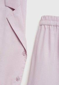 Set di tessuti morbidi di color viola chiaro composto da una camicia con bottoni e pantaloni con vita elastica. Texture morbida, finitura liscia e dettagli di design su misura.