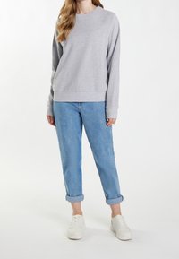 Sudadera gris claro con mangas largas, cuello redondo y puños acanalados, combinada con jeans azul claro remangados y zapatillas blancas.