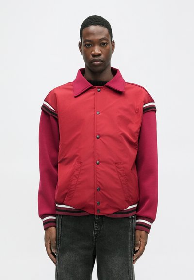Rdeča in maroon bomber jakna z gumbki na pritrditev, rebrastimi manšeti in dvema stranskima žepoma. Ima črtaste poudarke na rokavu.