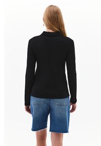 Schwarzes Langarmoberteil mit Kragen, kombiniert mit blauen Jeansshorts, die einen ausgefransten Saum und normale hintere Taschen aufweisen.