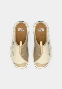 Lette, slip-on sko med en beige mesh-overdel med en teksturert overflate, korksåle og subtil merkevare på siden og hælen.