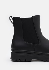 Czarne botki za kostkę z gładkiej skórzanej cholewki, z elastycznymi panelami bocznymi i teksturowaną gumową podeszwą. Pętelka do zakładania z tyłu.