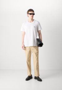Hvit bomulls T-skjorte med en liten svart logo, parret med beige rette bukser og svarte loafers, holder en svart veske.