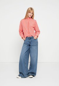Red and white gingham button-up shirt paired with wide-leg light blue denim jeans and black and white sneakers. Smooth fabric and ample fit.