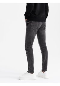 Jeans de denim gris de corte slim con un acabado deslavado, que cuentan con bolsillos traseros y se combinan con zapatillas blancas. Tejido texturizado con detalles sutiles.