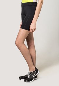 Shorts de sport noirs avec une taille haute, arborant un logo Nike, associés à des chaussures de course noires et grises avec des accents blancs.