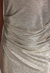Metallisk silverfärgad klädestyg med en texturerad yta, som har draperade detaljer som skapar mjuka veck och samlingar över materialet.