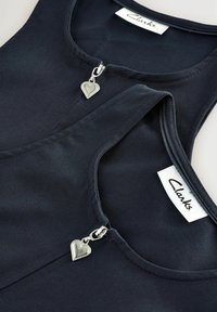 Jūras zila apģērbs ar apaļu dekoltē, kura priekšpusē ir rāvējslēdzis, papildināts ar mazu sudraba sirds formas piekariņu un "Clarks" etiķeti.