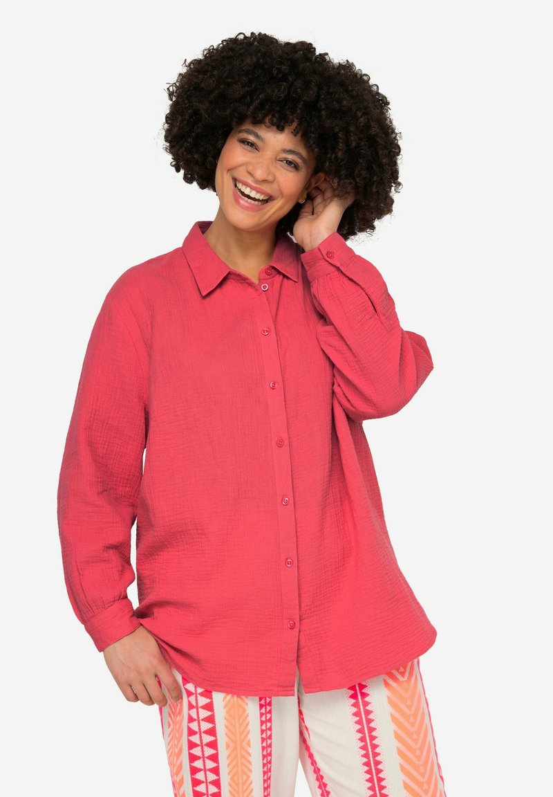 Rosa Hemdbluse aus strukturiertem Stoff mit Kragen und langen Ärmeln. Auffällige Knopfdetails verlaufen entlang der Vorderseite.