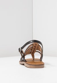 Sandalia de cuero negro con múltiples correas, parte trasera abierta y suela marrón. La correa del tobillo ajustable cuenta con una hebilla plateada. Plantilla texturizada.