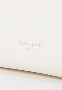 White leather wallet featuring the text "kate spade NEW YORK" embossed in silver. Smooth texture with minimalistic design.