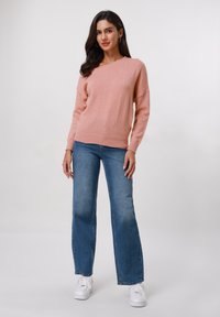 Pull en tricot rose avec une coupe décontractée, un large col, et un ourlet côtelé, associé à un jean en denim bleu évasé et des baskets blanches.