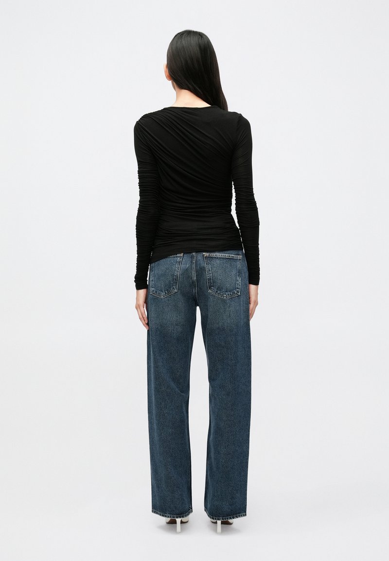 Sort langærmet top med rulletekstur, kombineret med højtaljede, vide blå jeans. Glat stof, afslappet pasform og ensfarvede baglommer.