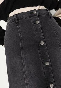 Svart denimkjol med silverfärgade knappstängningar, sömdetaljer på frampanelen och en figursydd siluett. Mjuk textur och medellång design.