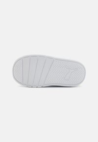 Semelle de sneaker blanche avec un motif de grip texturé, comprenant des designs en vagues et en zigzags, avec un estampillage de logo près de la zone du talon.