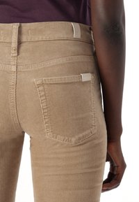 Brown corduroy jeans with a textured, ribbed design. Features a back pocket with a tag and a snug fit around the waist and hips.
