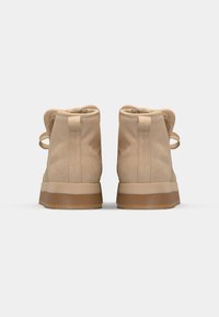 Stivaletti alla caviglia in suede beige con una morbida fodera interna, forma arrotondata e una robusta suola in gomma marrone. Presentano anelli in tessuto per facilitare l'indossamento.