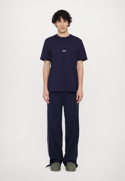 Maglietta in cotone blu navy con colletto tondo e logo bianco "MSG", abbinata a pantaloni larghi coordinati con strisce laterali bianche.