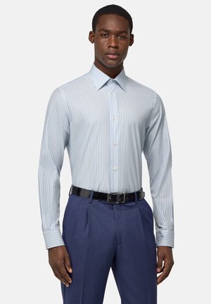 Camisa de vestir a rayas en azul claro y blanco, con cuello, mangas largas y apertura con botones. Se lleva con pantalones oscuros azules y un cinturón negro.