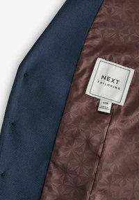 Blazer de marine con exterior texturizado, forro con patrón en burdeos y etiqueta cosida que dice "NEXT TAILORING", tamaño 40R, hecho en Bangladesh.