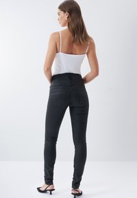 Zwarte skinny jeans met hoge taille en een gladde, rekbare textuur, met twee achterzakken en een ritssluiting. Gekoeld met een witte tanktop.