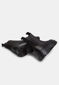 Botas negras hasta el tobillo con un acabado de cuero suave, paneles laterales elásticos y suelas de goma texturizadas con ranuras profundas para una mejor tracción.