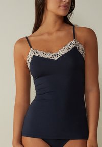 Débardeur bleu marine avec un délicat bord en dentelle crème le long du décolleté, doté de fines bretelles et d'une silhouette ajustée. Tissu lisse, sans motifs.